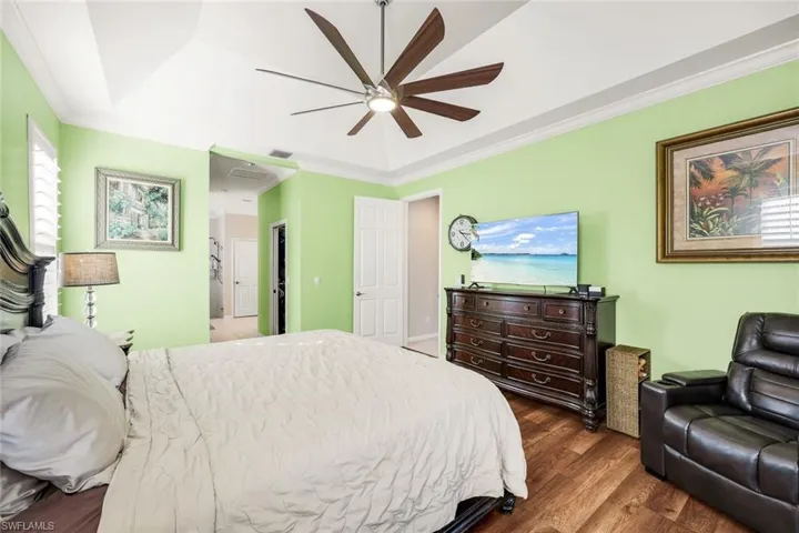 Bedroom with a tray ceiling, ornamental molding, dark wood-type flooring, and ceiling fan