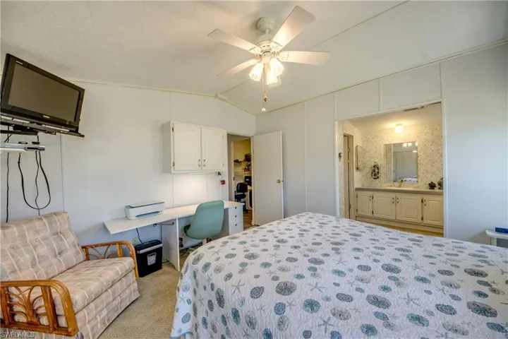 Carpeted bedroom featuring ceiling fan, ensuite bathroom, vaulted ceiling, and ornamental molding
