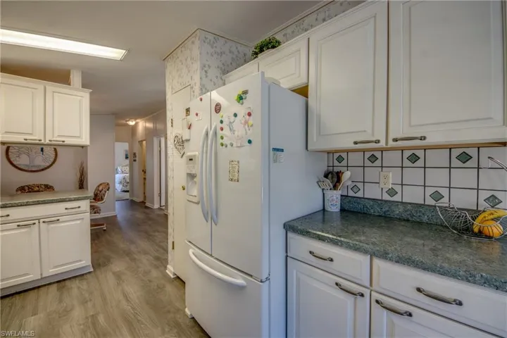 Kitchen featuring white cabinets, decorative backsplash, light hardwood / wood-style floors, and white fridge with ice dispenser