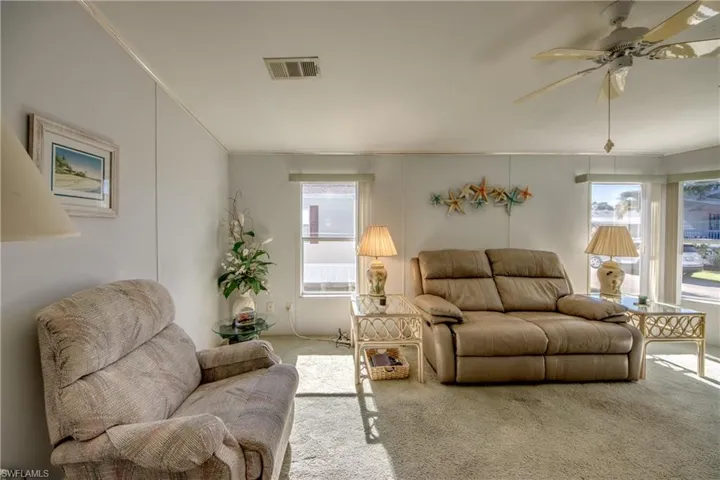 Carpeted living room with ceiling fan, ornamental molding, and a wealth of natural light