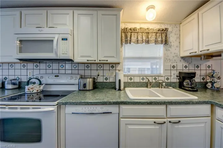 Kitchen with backsplash, white cabinetry, white appliances, and sink