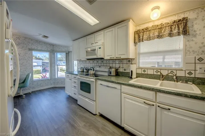 Kitchen featuring white cabinetry, sink, a healthy amount of sunlight, and white appliances