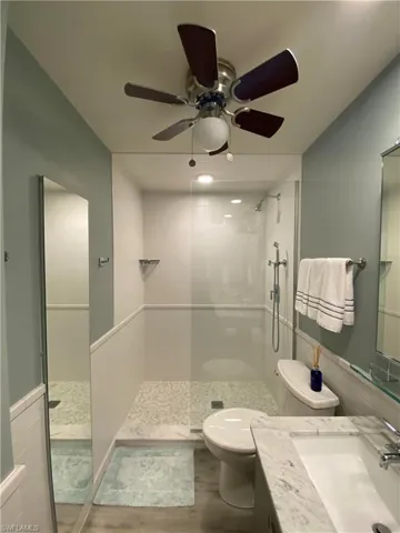 Bathroom with vanity, toilet, ceiling fan, and a tile shower