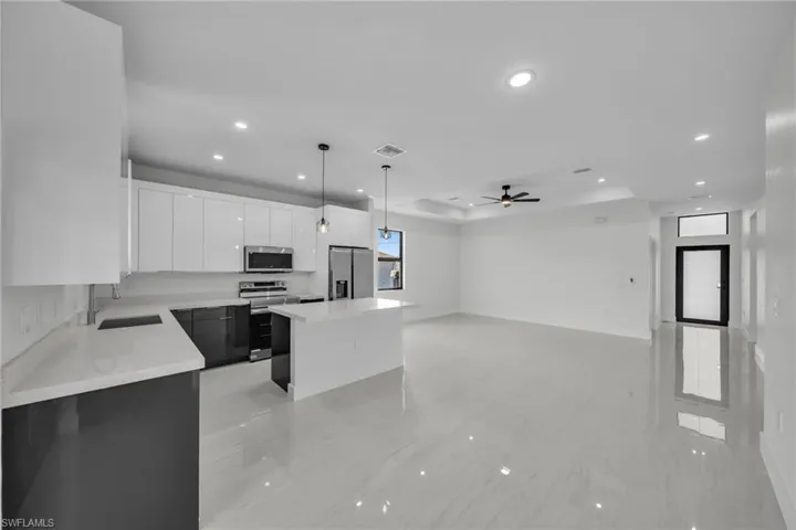 Kitchen featuring white cabinets, hanging light fixtures, a tray ceiling, appliances with stainless steel finishes, and a center island