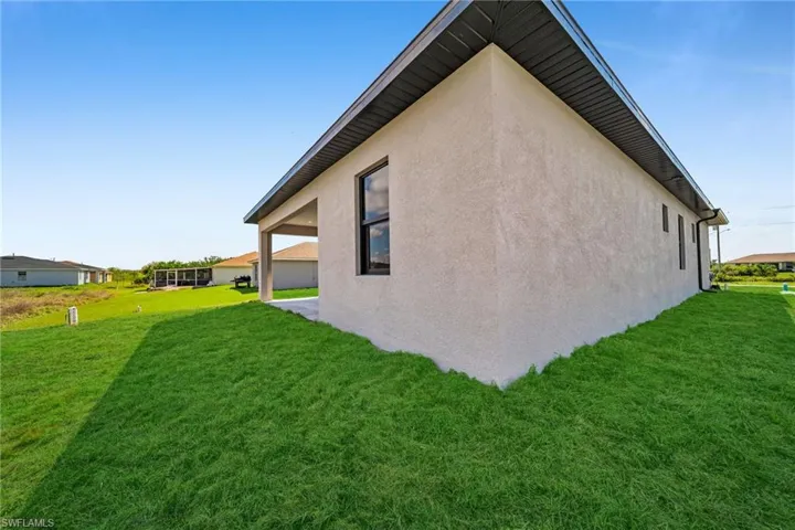 View of side of property featuring a lawn, stucco siding, and a patio