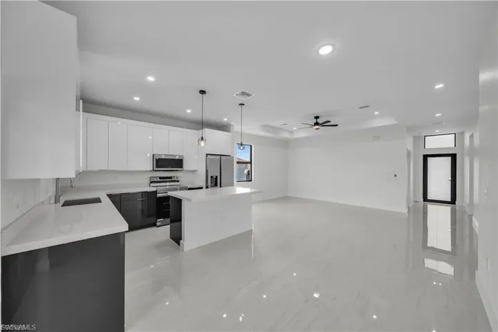 Kitchen with white cabinets, decorative light fixtures, a tray ceiling, appliances with stainless steel finishes, and a kitchen island