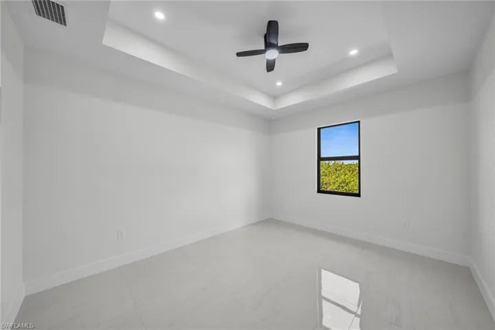 Empty room with a raised ceiling, recessed lighting, and a ceiling fan