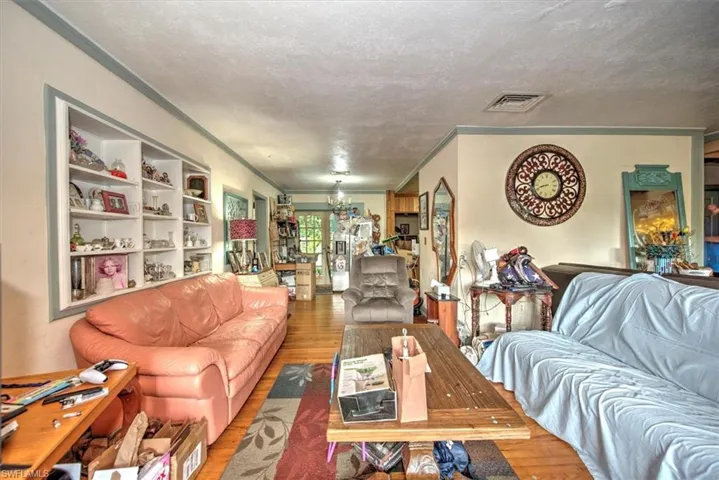Living room featuring a textured ceiling, ornamental molding, built in shelves, and hardwood / wood-style flooring