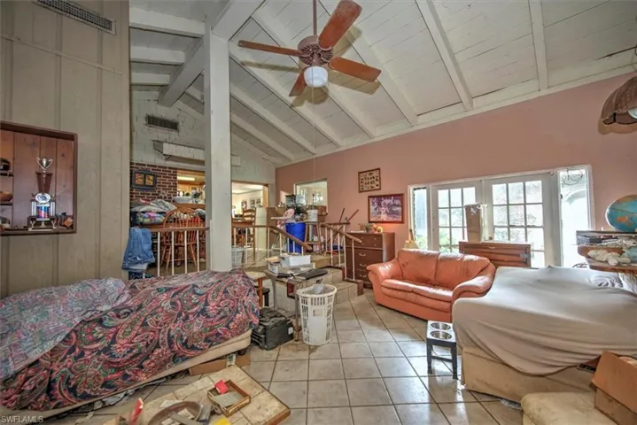 Bedroom featuring brick wall, light tile patterned floors, beam ceiling, high vaulted ceiling, and ceiling fan