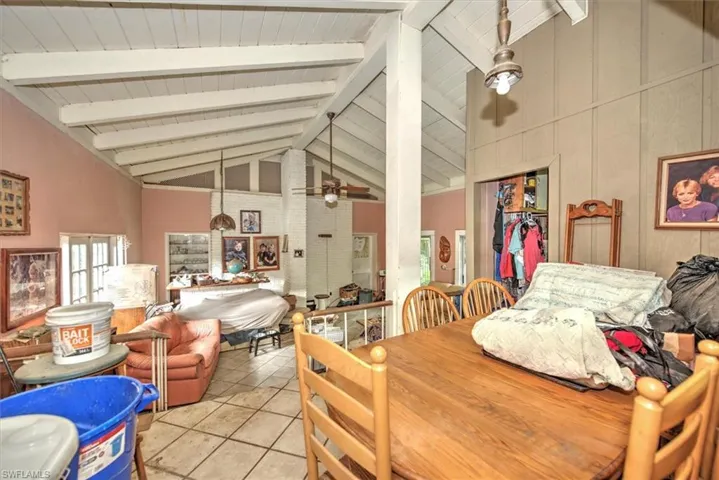 Dining space with beamed ceiling, ceiling fan, brick wall, light tile patterned flooring, and high vaulted ceiling