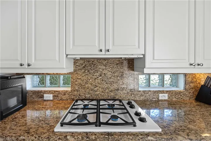 Kitchen with white cabinetry, tasteful backsplash, white gas stovetop, and dark stone countertops