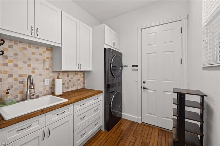 Laundry room with dark wood-type flooring, cabinets, stacked washing maching and dryer, and sink