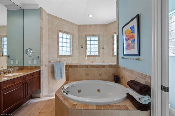 Primary bathroom with vanity, ornamental molding, a relaxing jacuzzi tub, and tile patterned floors