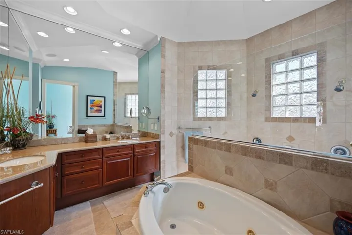 Primary Bathroom with a healthy amount of sunlight, vanity, vaulted ceiling, and tile walls