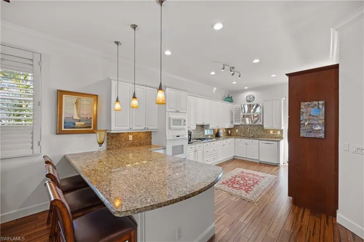 Kitchen with decorative light fixtures, white cabinetry, a kitchen bar, kitchen peninsula, and white appliances