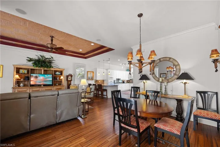 Dining room with a tray ceiling, ceiling fan with notable chandelier, ornamental molding, and hardwood / wood-style flooring
