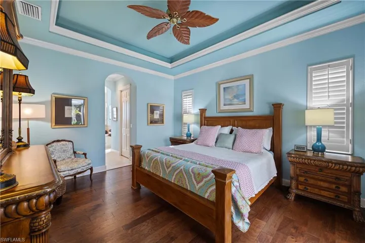 Primary bedroom with ceiling fan, ornamental molding, dark hardwood / wood-style flooring, and a raised ceiling