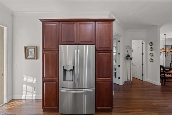 Kitchen featuring dark hardwood / wood-style flooring, stainless steel fridge with ice dispenser, ornamental molding, and a chandelier