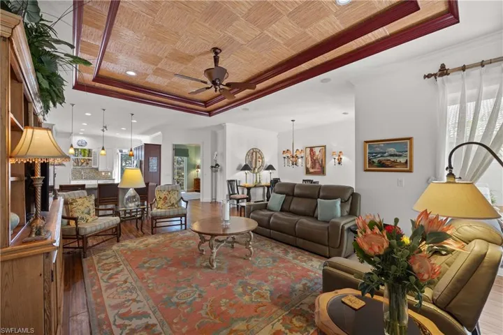 Living room with ceiling fan with notable chandelier, ornamental molding, a raised ceiling, and hardwood / wood-style floors