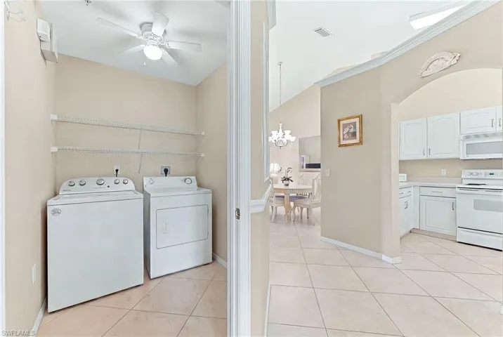 Laundry area featuring light tile patterned floors, ornamental molding, a ceiling fan, hanging lights, and independent washer and dryer