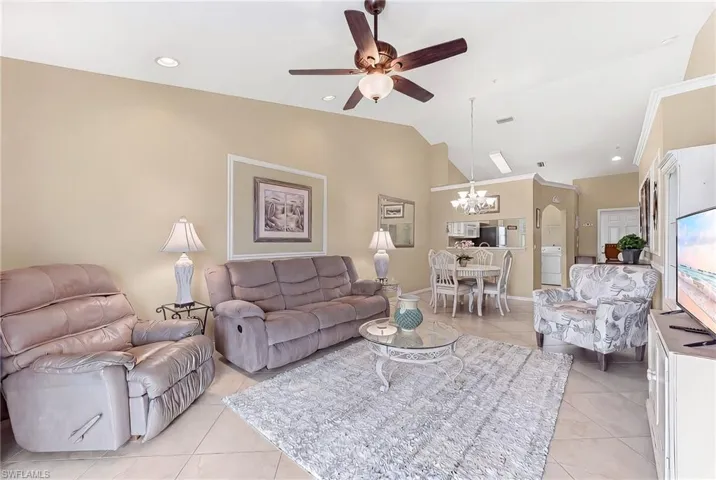 Living room featuring ceiling fan, light tile patterned flooring, hanging lights, and vaulted ceiling