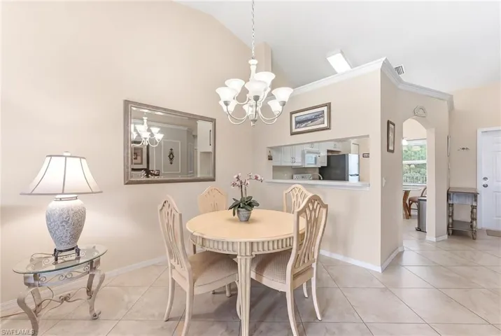 Dining area featuring arched walkways, vaulted ceiling, light tile patterned floors, hanging lights, and ornamental molding
