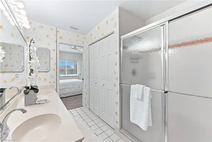 Full bath with double vanity, ensuite bath, a closet, a stall shower, and wallpapered walls
