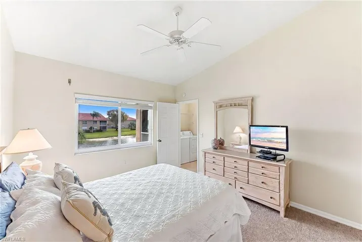 Bedroom with vaulted ceiling, light colored carpet, washing machine and dryer, and a ceiling fan