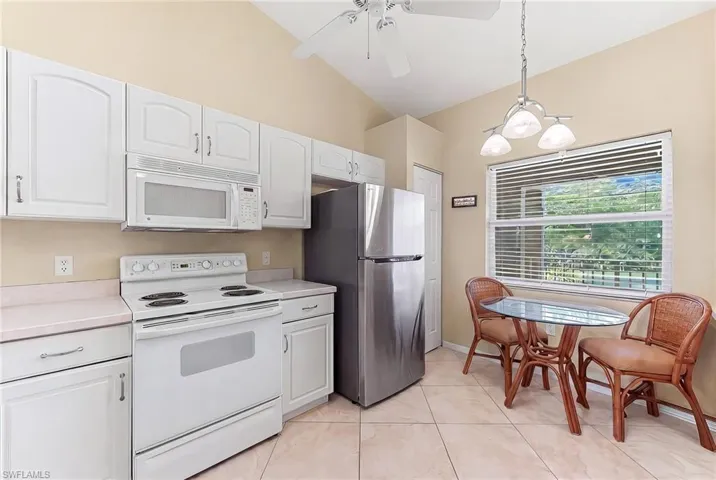 Kitchen with white appliances, light countertops, hanging light fixtures, white cabinetry, and lofted ceiling