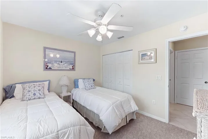 Bedroom with a closet, light carpet, ceiling fan, and light tile patterned floors