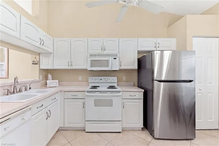 Kitchen with white appliances, white cabinetry, light countertops, a ceiling fan, and a high ceiling