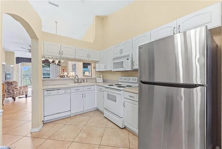 Kitchen with white appliances, light countertops, white cabinetry, light tile patterned floors, and vaulted ceiling