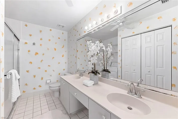 Full bath with wallpapered walls, a ceiling fan, double vanity, and a shower stall