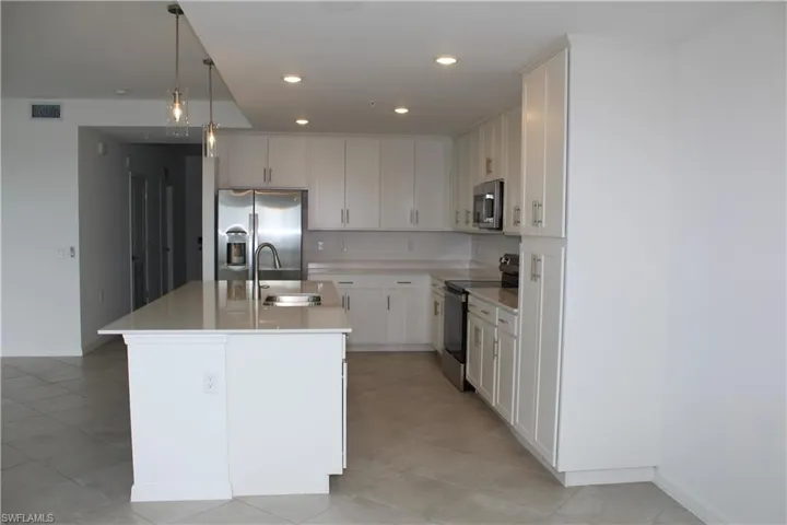 Kitchen with stainless steel appliances, a sink, light countertops, a kitchen island with sink, and light tile patterned flooring