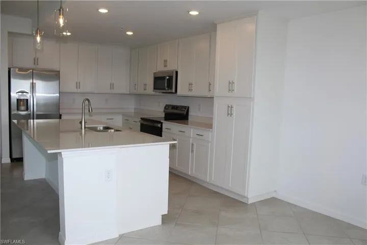 Kitchen with stainless steel appliances, a sink, an island with sink, light tile patterned floors, and recessed lighting