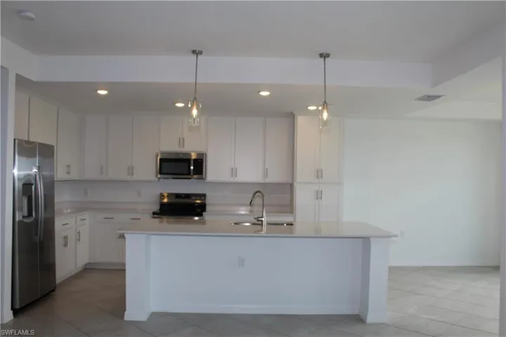 Kitchen with appliances with stainless steel finishes, a sink, light countertops, recessed lighting, and white cabinetry