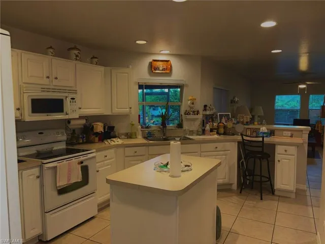 Kitchen featuring white appliances, a peninsula, light countertops, light tile patterned flooring, and white cabinets