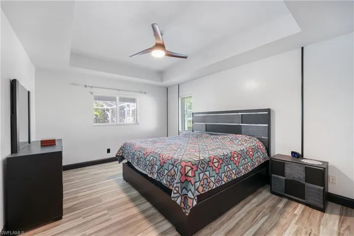 Bedroom with a raised ceiling, a ceiling fan, and light wood finished floors