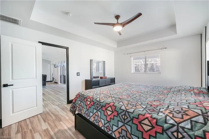 Bedroom with a tray ceiling, light wood finished floors, and ceiling fan