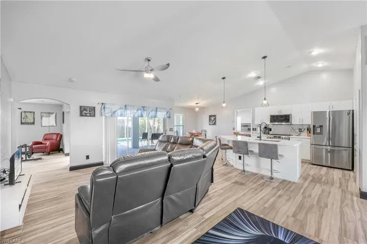 Living area with lofted ceiling, light wood-style floors, arched walkways, and a ceiling fan