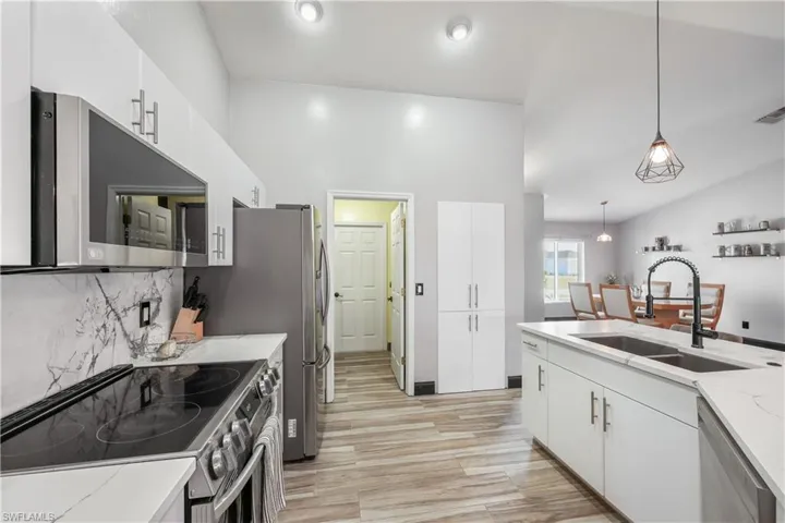 Kitchen with appliances with stainless steel finishes, pendant lighting, white cabinetry, light wood finished floors, and backsplash