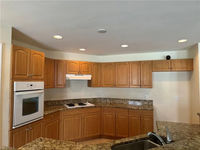 Kitchen with light tile patterned flooring, dark stone counters, white appliances, and sink