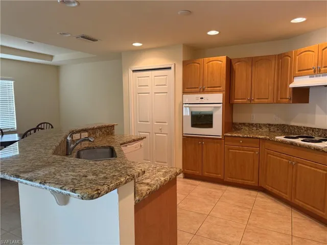 Kitchen with sink, a kitchen island with sink, light tile patterned floors, and white appliances