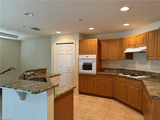 Kitchen with sink, light tile patterned floors, dark stone counters, and white appliances