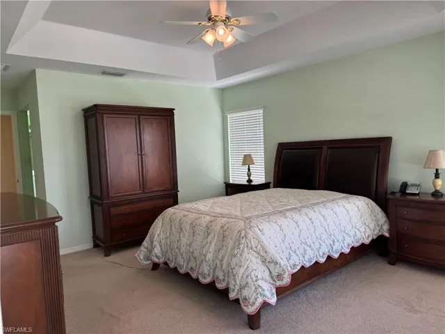 Bedroom with light carpet, ceiling fan, and a raised ceiling