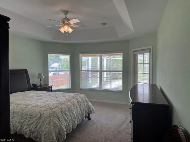 Bedroom with carpet floors, ceiling fan, and a raised ceiling