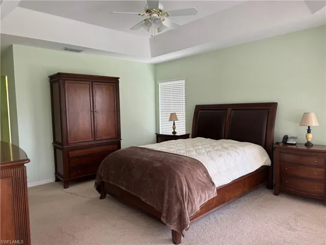 Carpeted bedroom with ceiling fan and a raised ceiling
