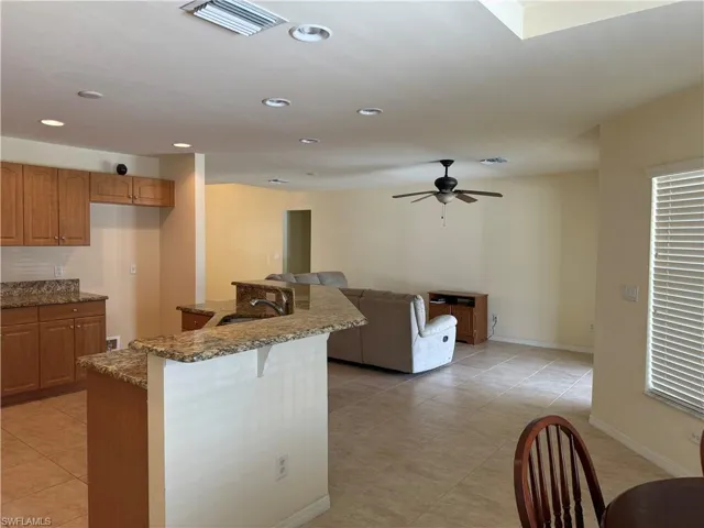 Kitchen with ceiling fan, sink, a breakfast bar, stone countertops, and light tile patterned floors