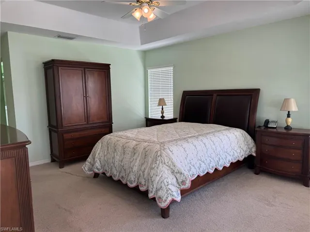 Bedroom with a tray ceiling, light carpet, and ceiling fan