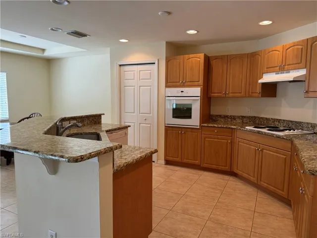 Kitchen featuring dark stone countertops, white appliances, light tile patterned floors, an island with sink, and sink